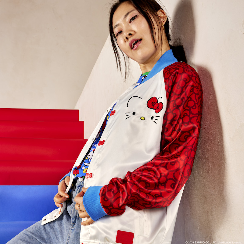Woman standing on red and blue stairs and wearing the Loungefly Sanrio Hello Kitty 50th Anniversary Unisex Souvenir Jacket 